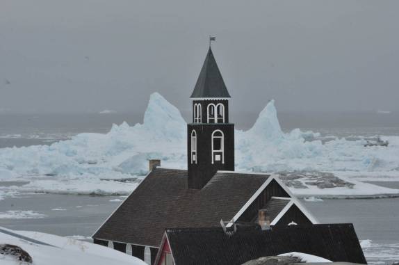 Zion Church, verdadeiro cartão postal de Ilulissat, na Groelândia. Ao fundo, icebergs passam pela costa.